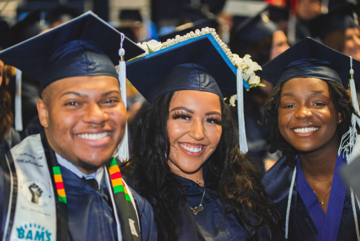 Three students in cap and gowns smile at the camera