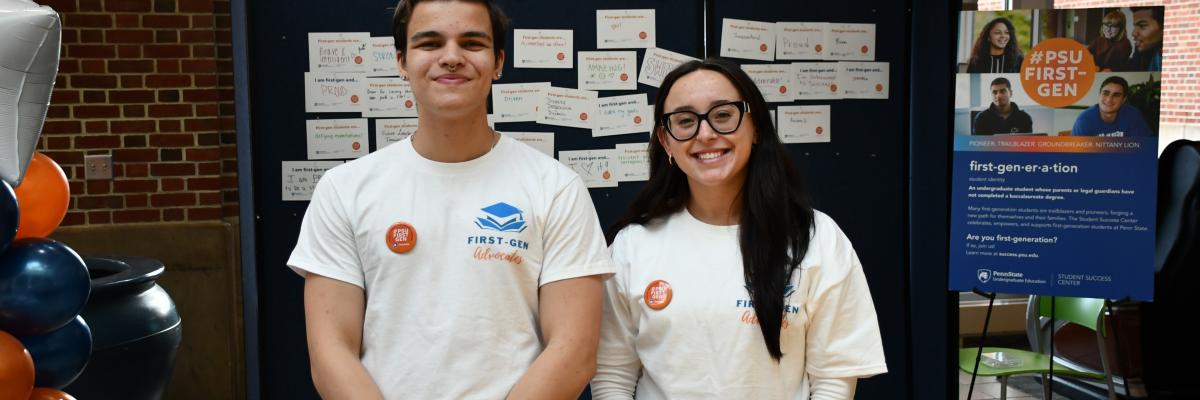 Two students standing behind a table wearing First-Gen Advocates shirts