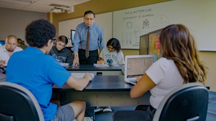 Students on laptops talking to a professor